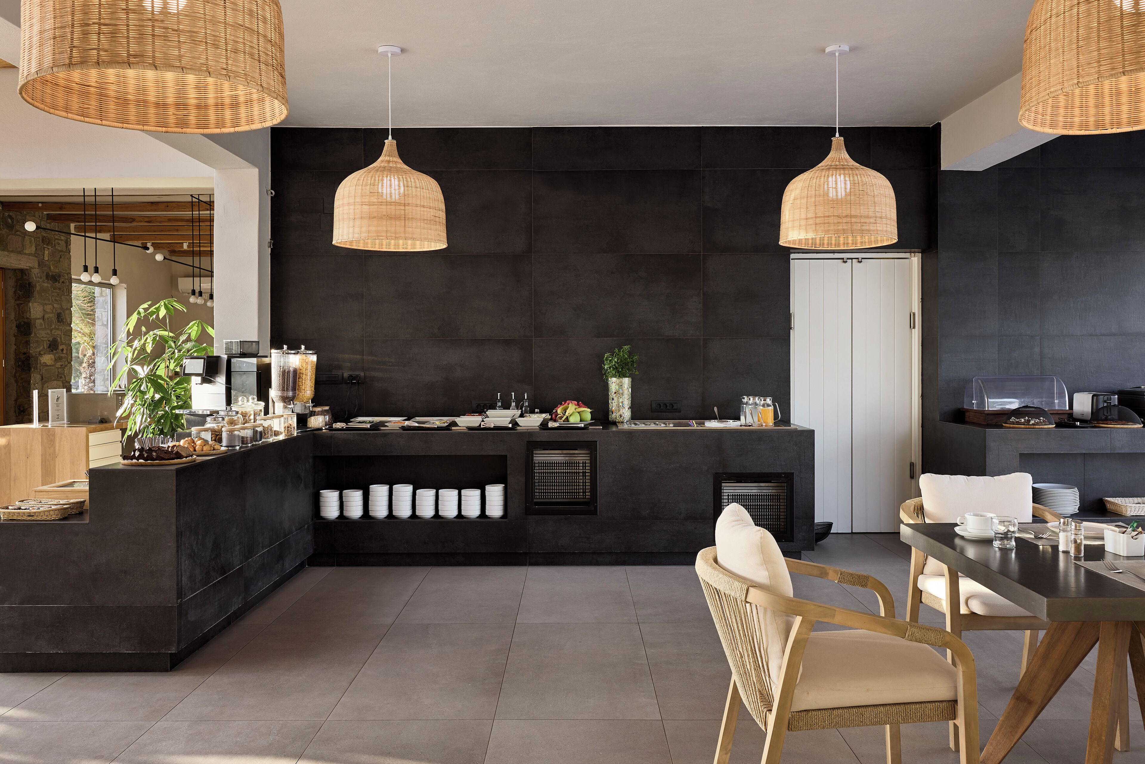 Une cuisine moderne avec des carreaux de couleur sombre, un îlot central doté d’un évier et trois suspensions en osier.