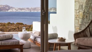 A modern outdoor seating area with a view of the sea, a stone wall, and a wooden bench. -  Hotel Milos Sea Resort (Milos)