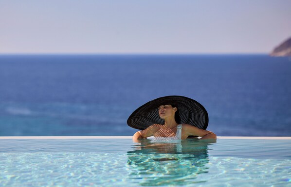Una persona en una piscina infinita transparente con vistas al océano.