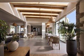 Un comedor amplio con vigas de madera, ventanas grandes y plantas en macetas.