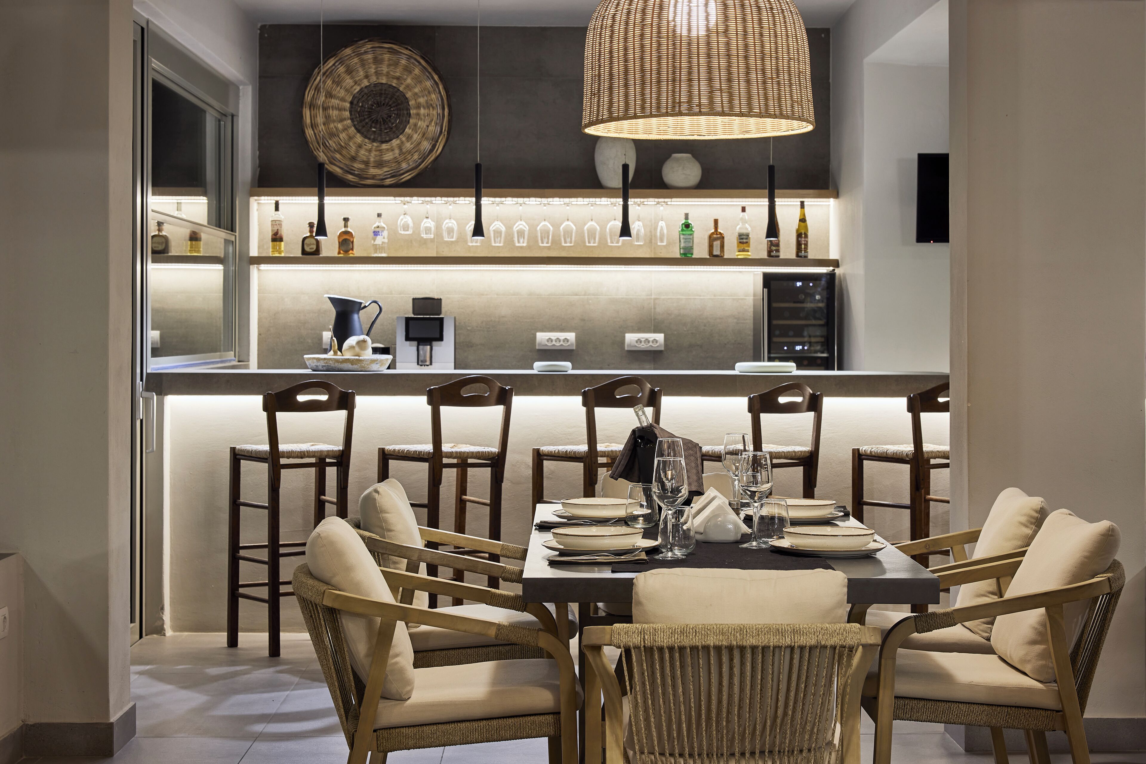 A dining area with a long table, chairs, and a bar area with bottles and glasses.