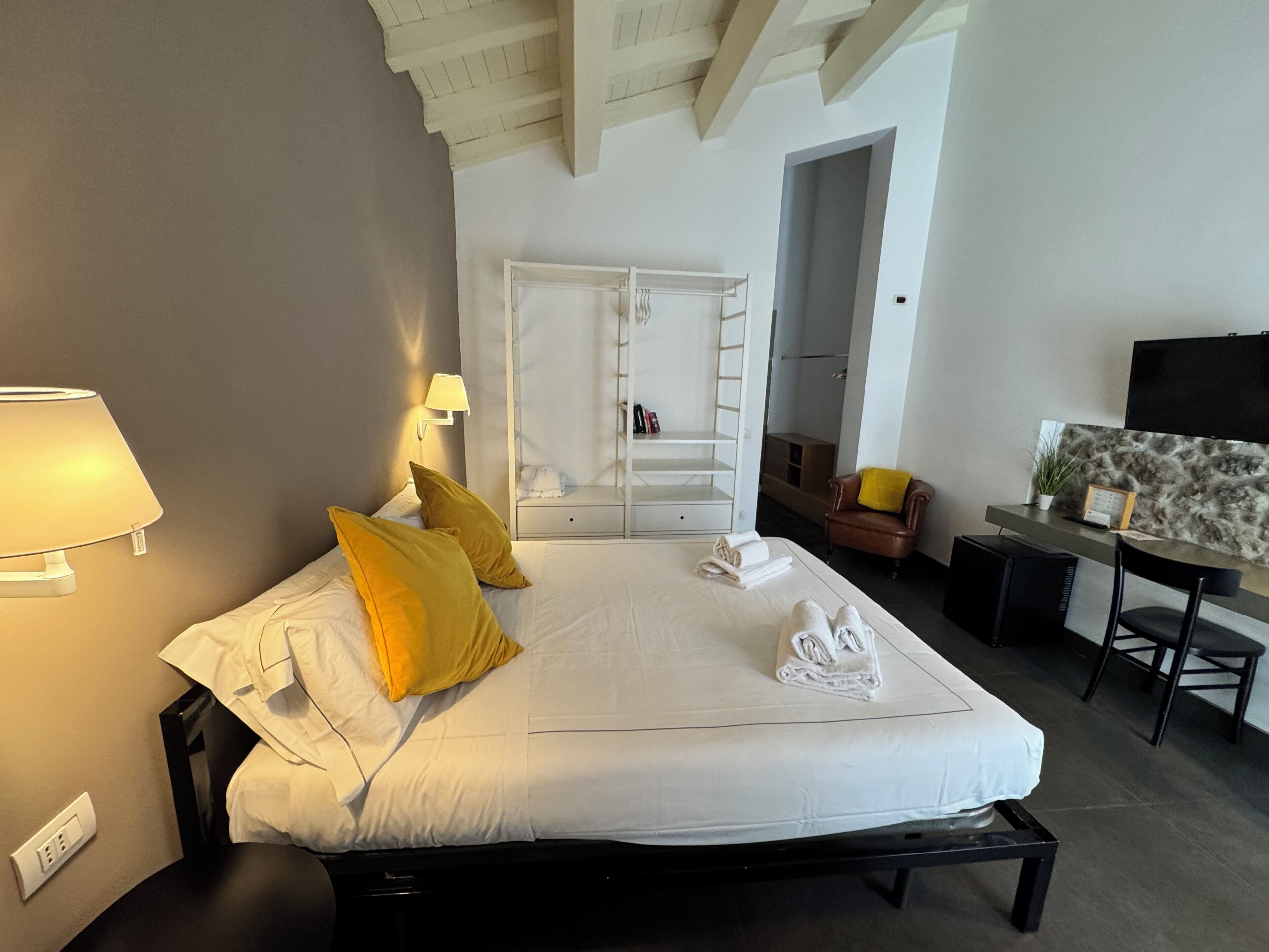 A hotel room with a bed, bedside lamp, a desk with a chair, a television, and a wardrobe.