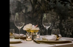 Mesa posta para refeição com duas taças de vinho, uma vela e um arranjo de flores.