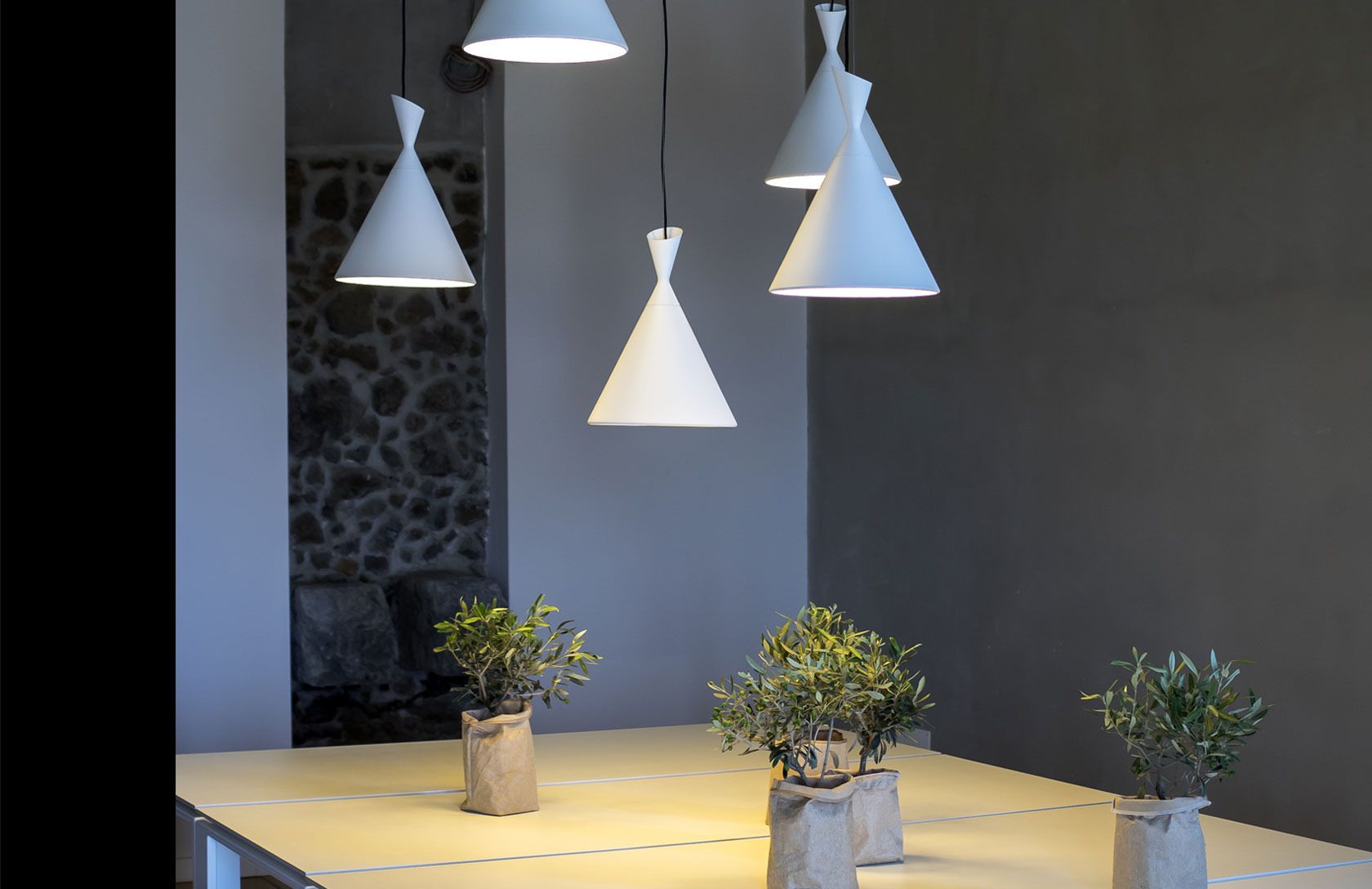 A modern interior with three pendant lights, a stone wall, and three potted plants on a table.