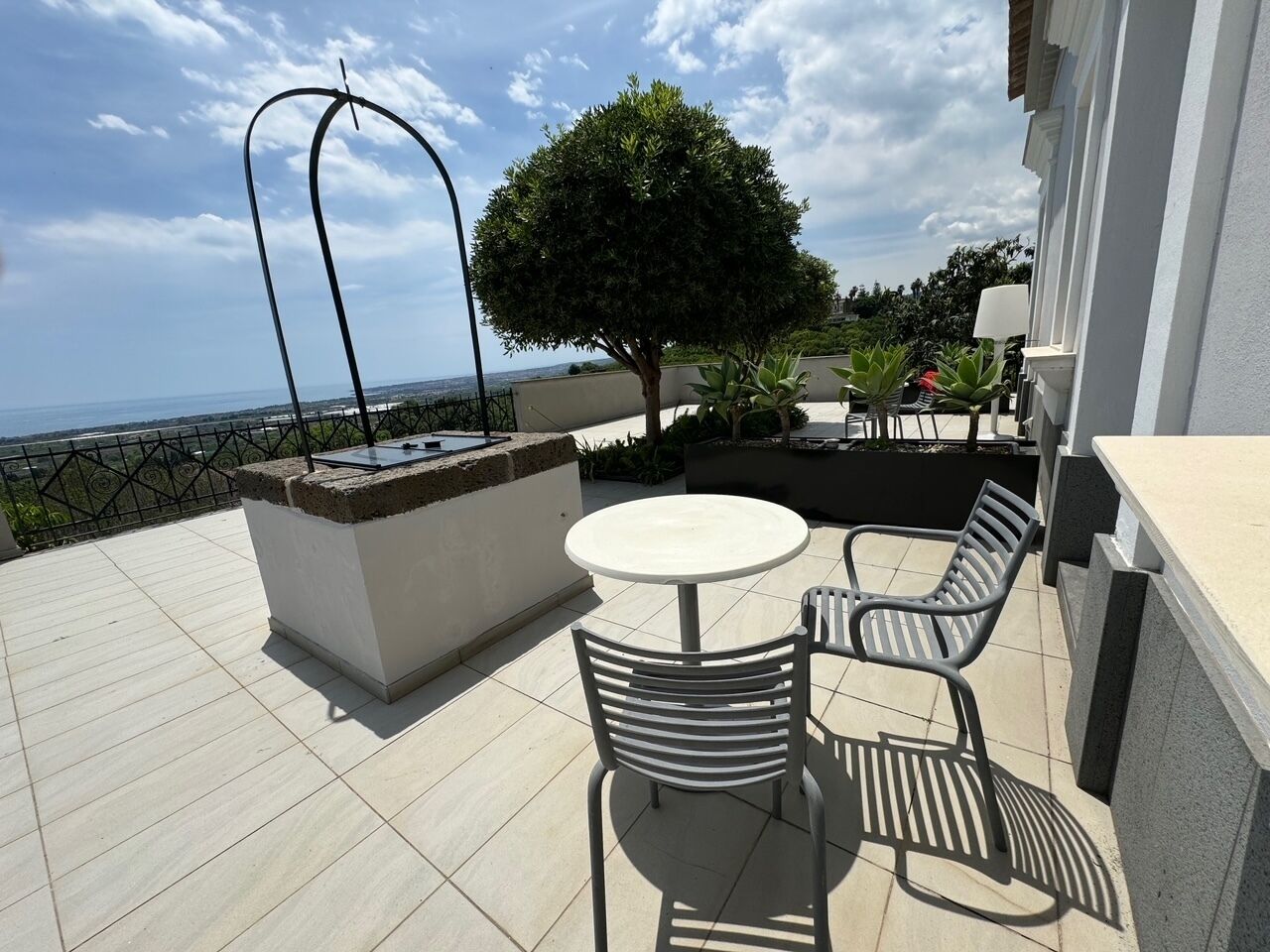Una terraza con mesa y sillas, un pequeño árbol y vistas al mar.