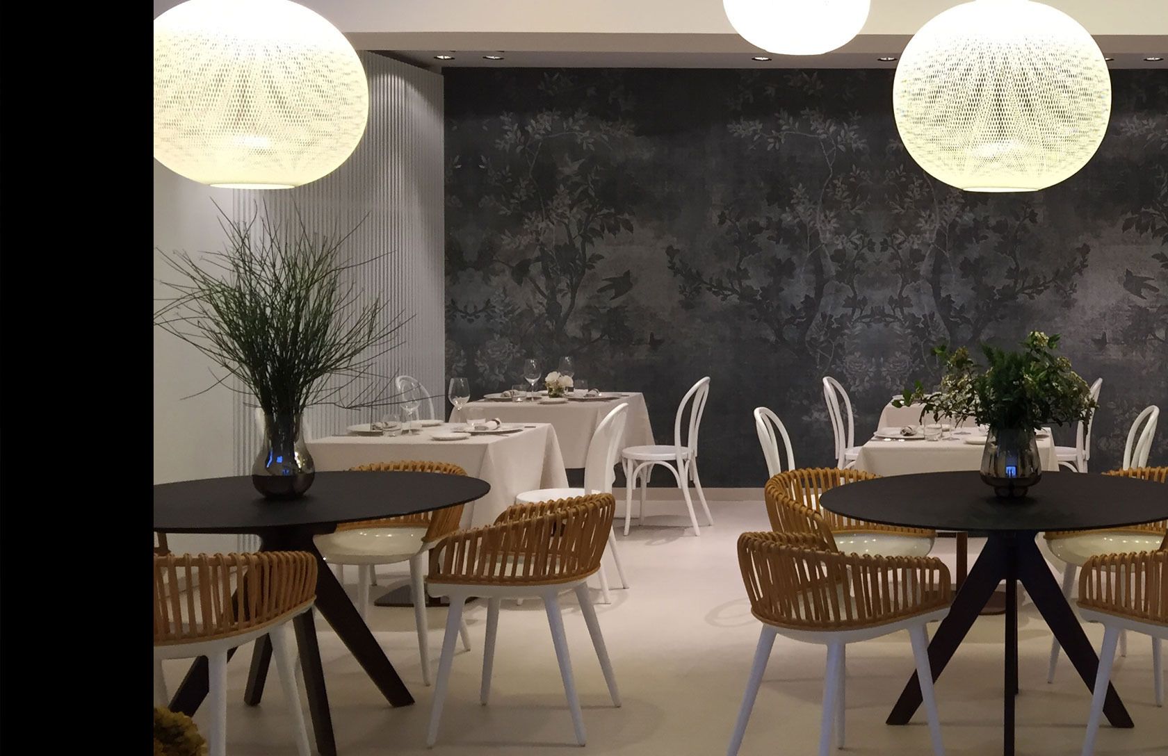 Un espace repas avec des tables rondes, des chaises en osier et des luminaires sphériques suspendus.