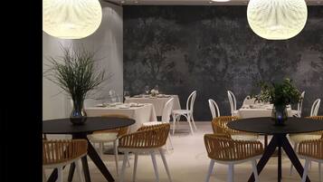 Un espace repas avec des tables rondes, des chaises en osier et des luminaires sphériques suspendus.