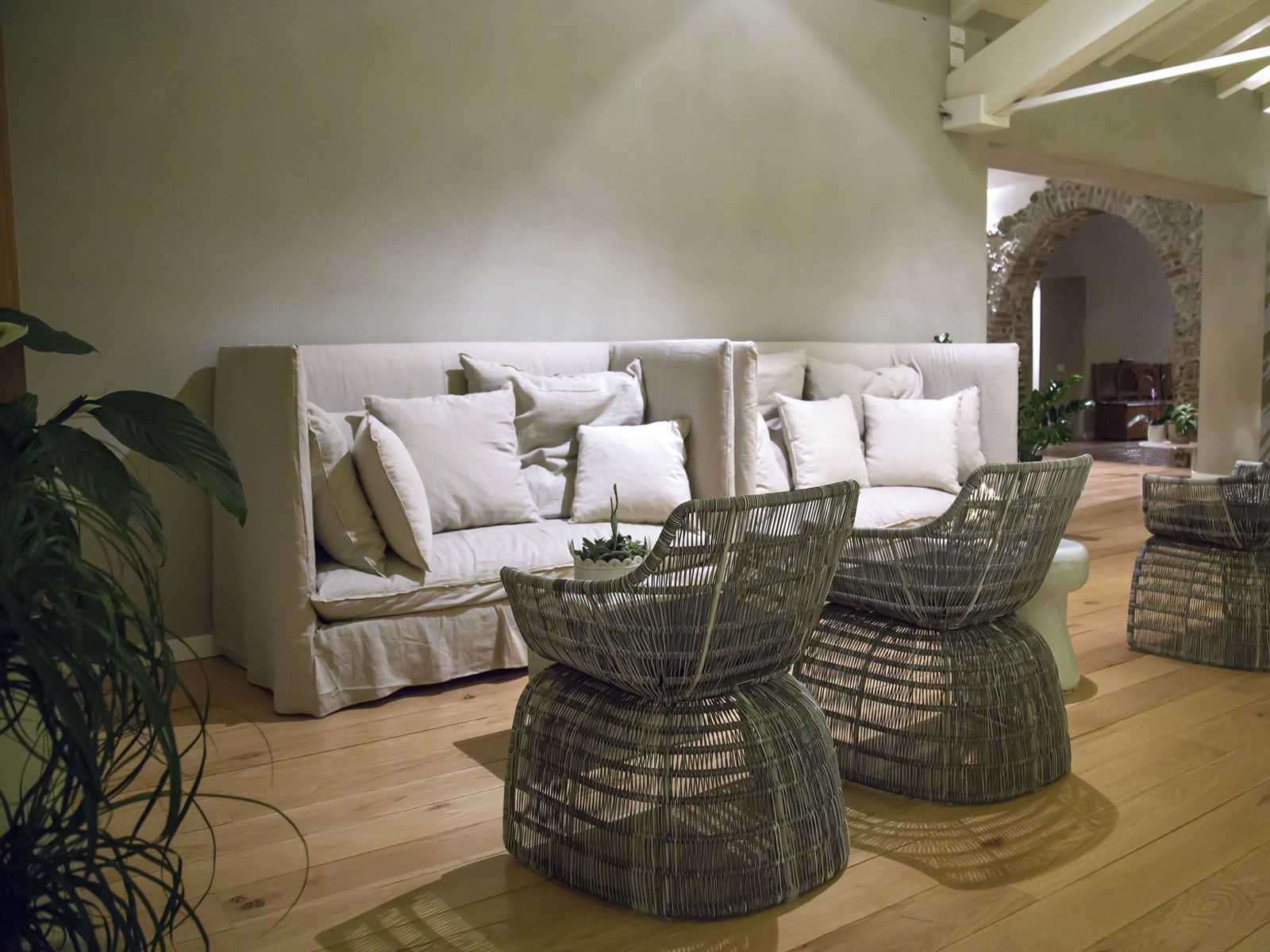 Een moderne woonkamer met een witte bank, rieten stoelen en een houten vloer.