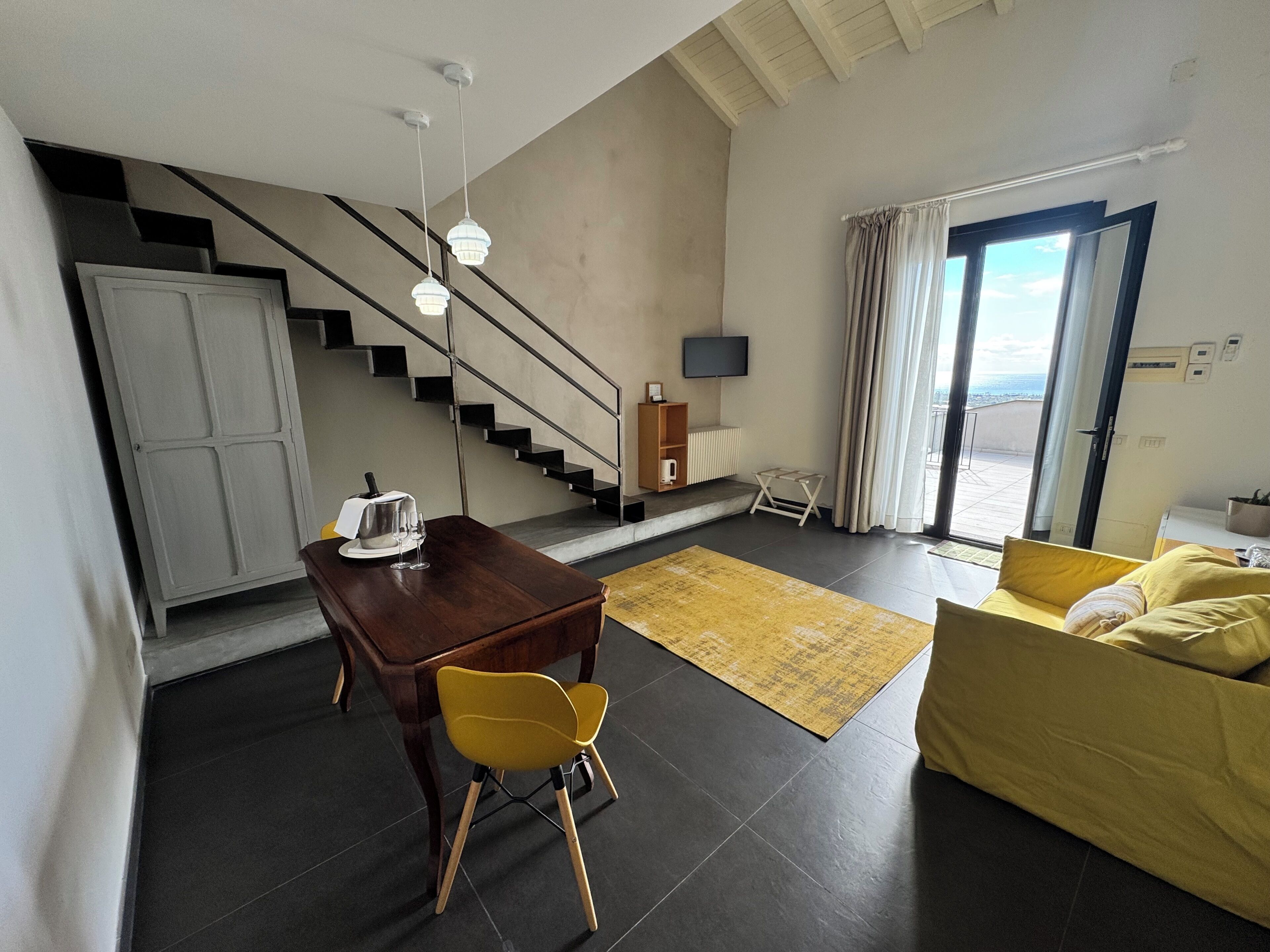 Ein moderner Wohnraum mit Treppe, Essbereich mit Tisch und Stühlen, Sofa, Fernseher und Blick durch eine Glastür.