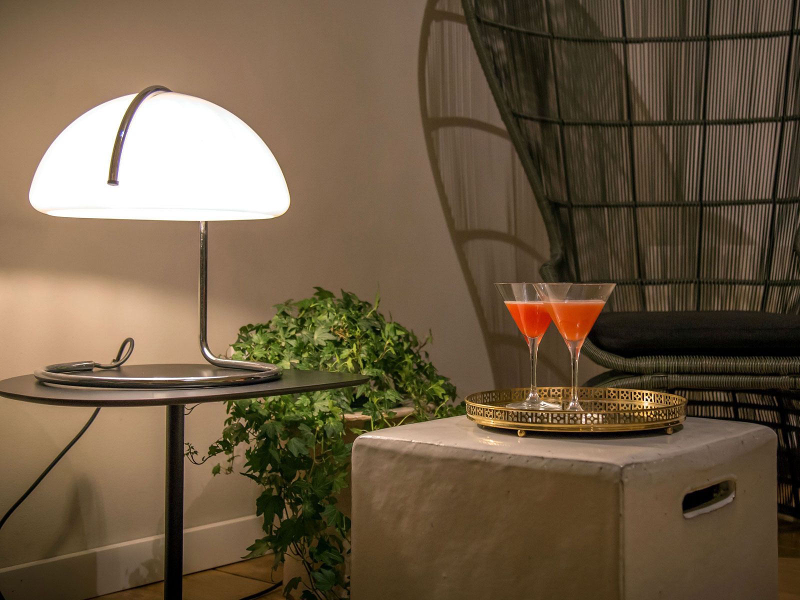 A lamp on a table, two martini glasses with a drink, and a plant.