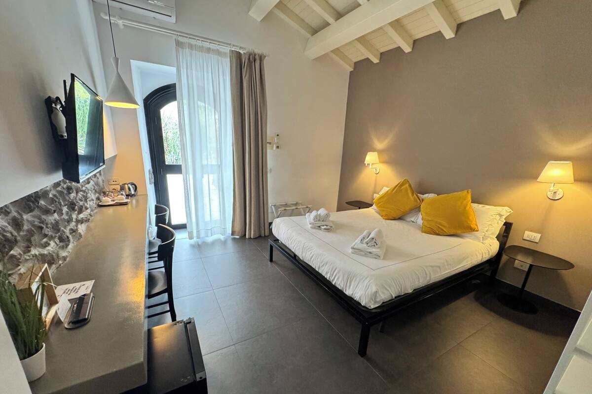 Habitación de hotel con cama, lámparas de noche, escritorio con silla, televisor y vistas al exterior.