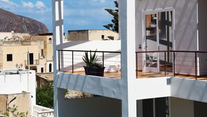 A modern building with a balcony, a potted plant, and a mountain in the background. - Resort Il Mulino (Favignana)