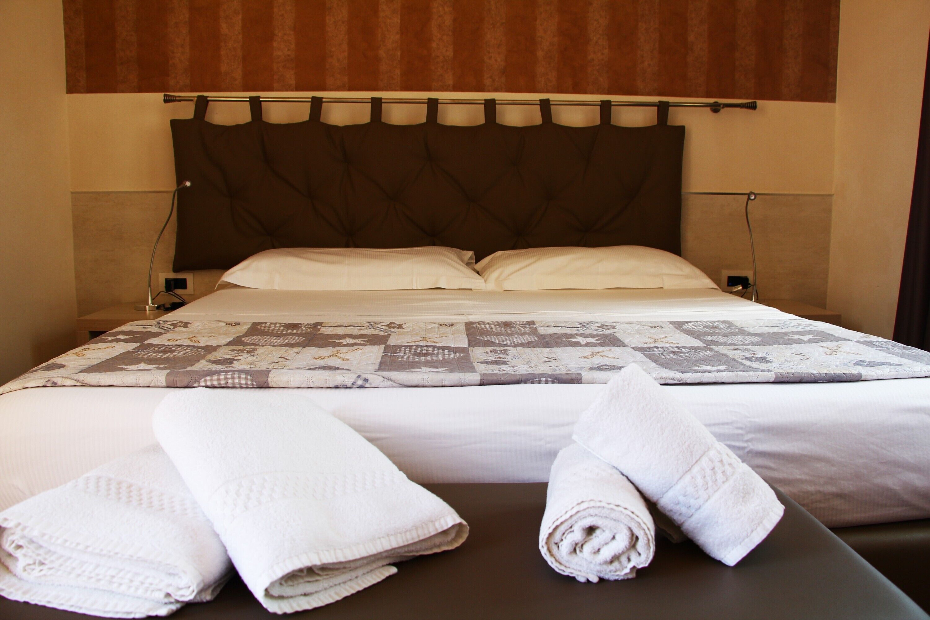 A neatly made bed with a quilt, two rolled towels, and a headboard.