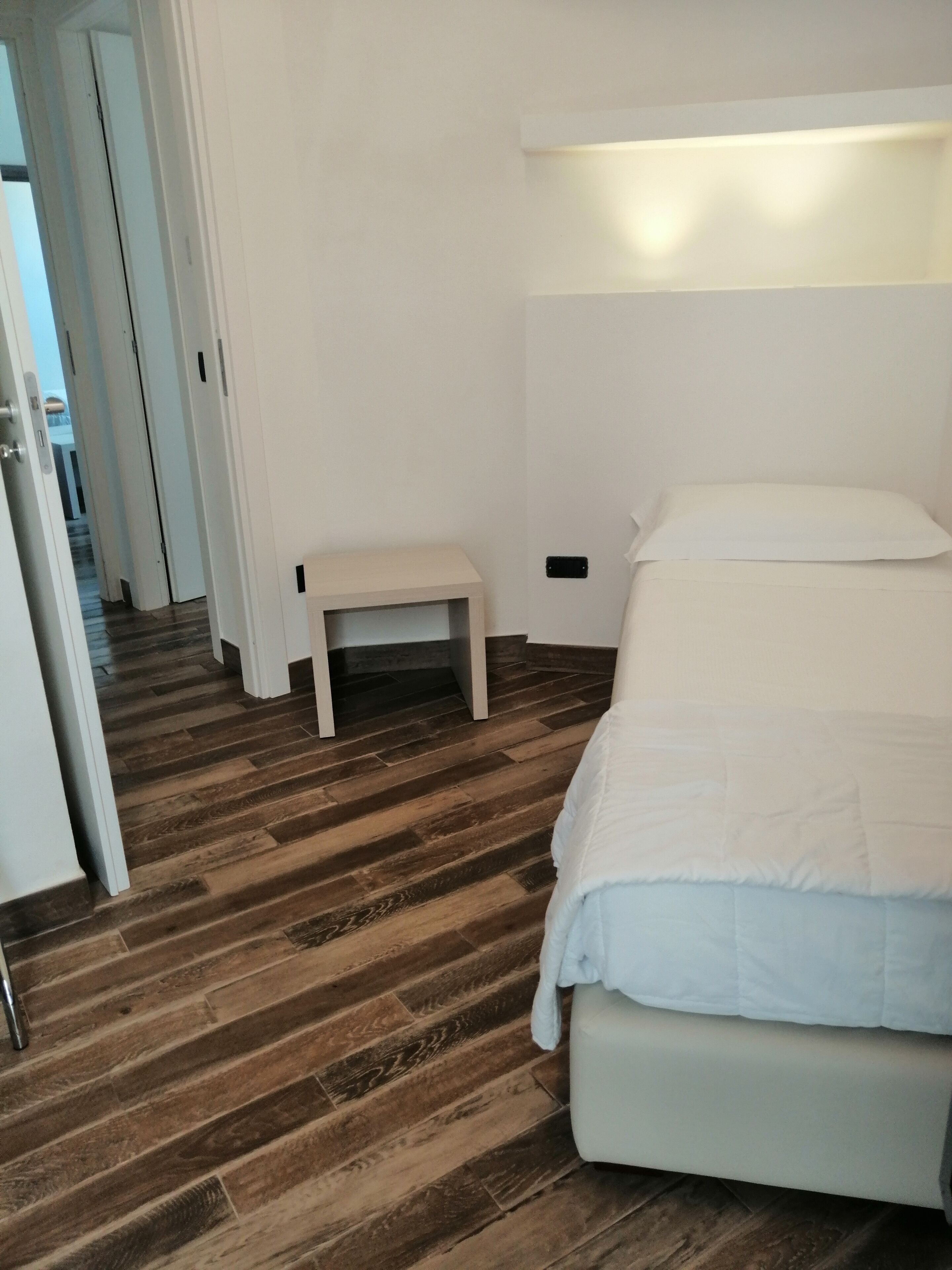 Une chambre avec un plancher en bois, un lit avec une literie blanche, une table de chevet et une petite table.