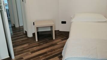 Une chambre avec un plancher en bois, un lit avec une literie blanche, une table de chevet et une petite table.