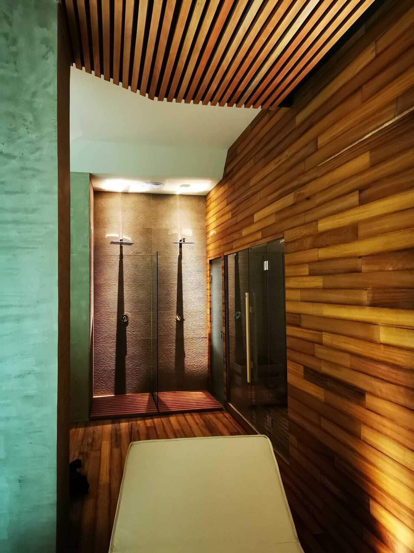 Un baño moderno con paneles de madera, cabina de ducha de vidrio y lavamanos blanco.