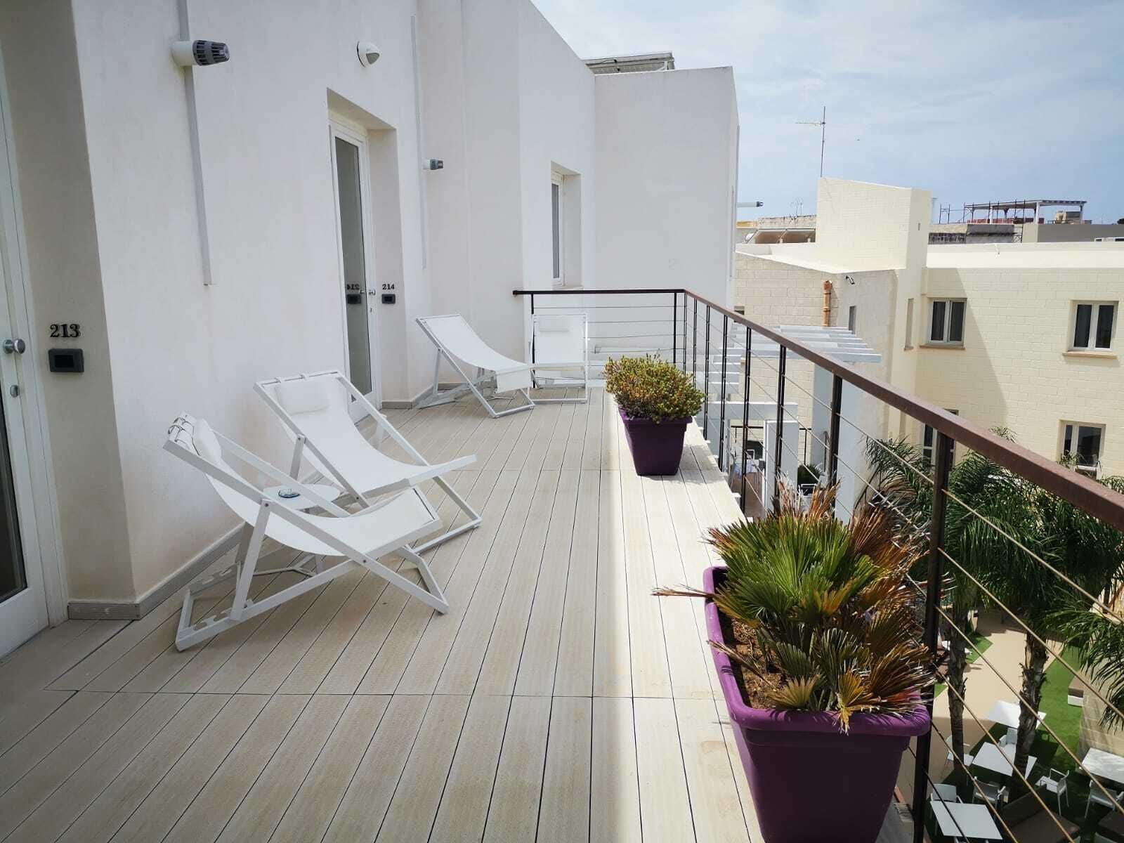 Un balcón con sillones blancos, una planta en maceta y vistas de edificios aledaños.