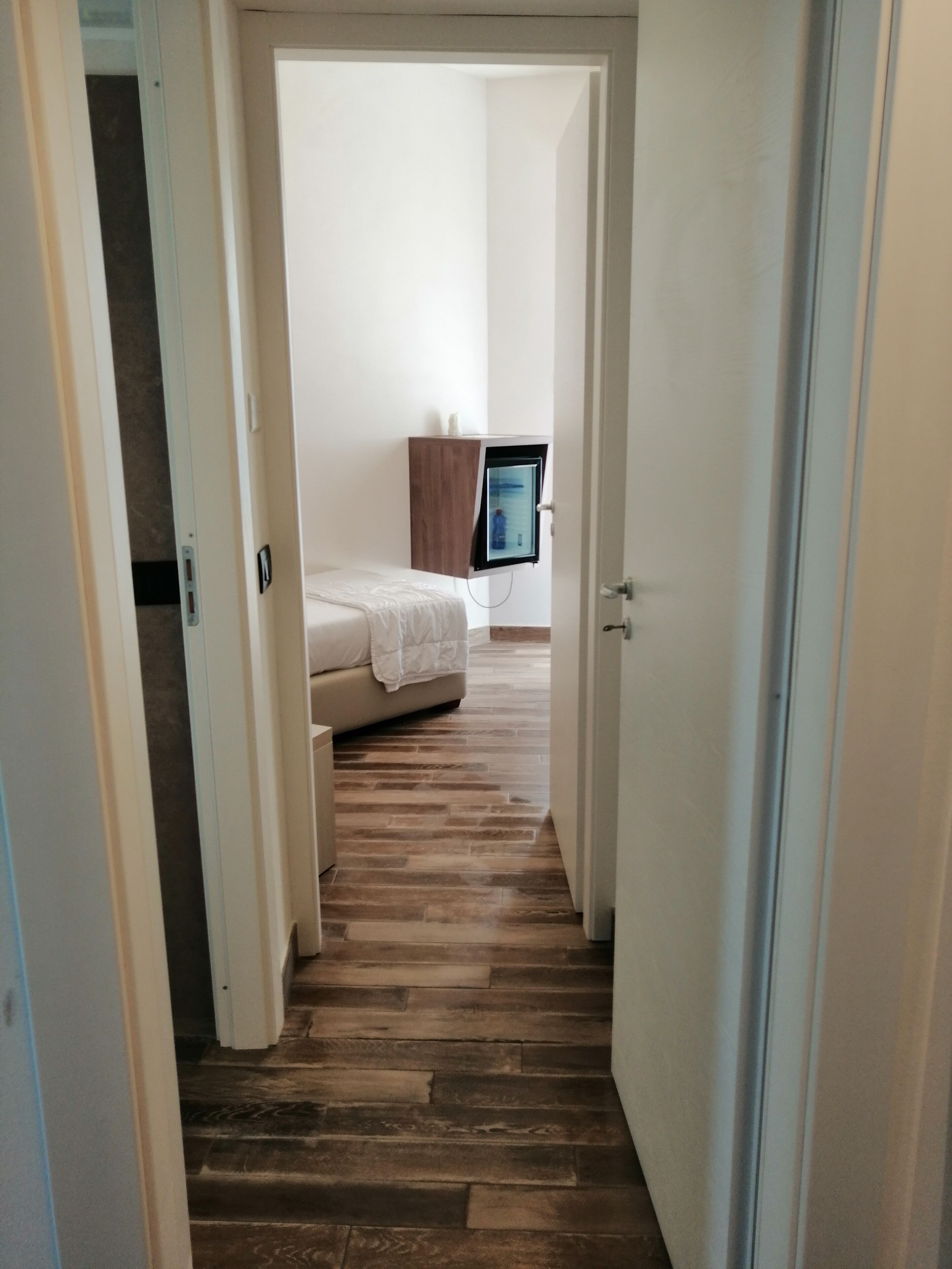 A narrow hallway with wooden flooring leading to a bedroom with a bed and a TV mounted on the wall.