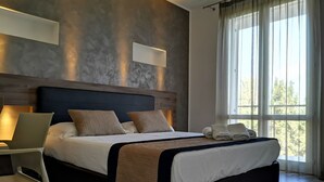 A modern hotel room with a large bed, a desk, and a window with curtains. - Resort Il Mulino (Favignana)