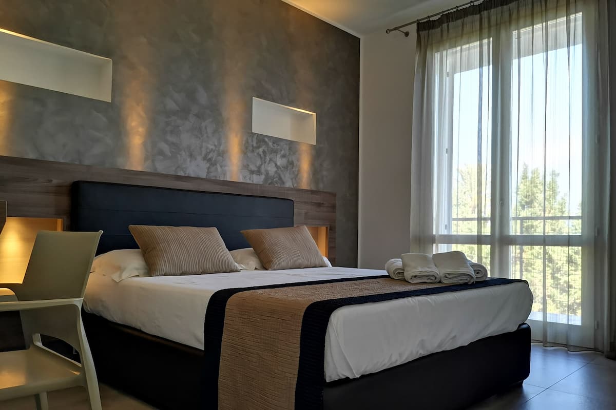 A modern hotel room with a large bed, a desk, and a window with curtains.