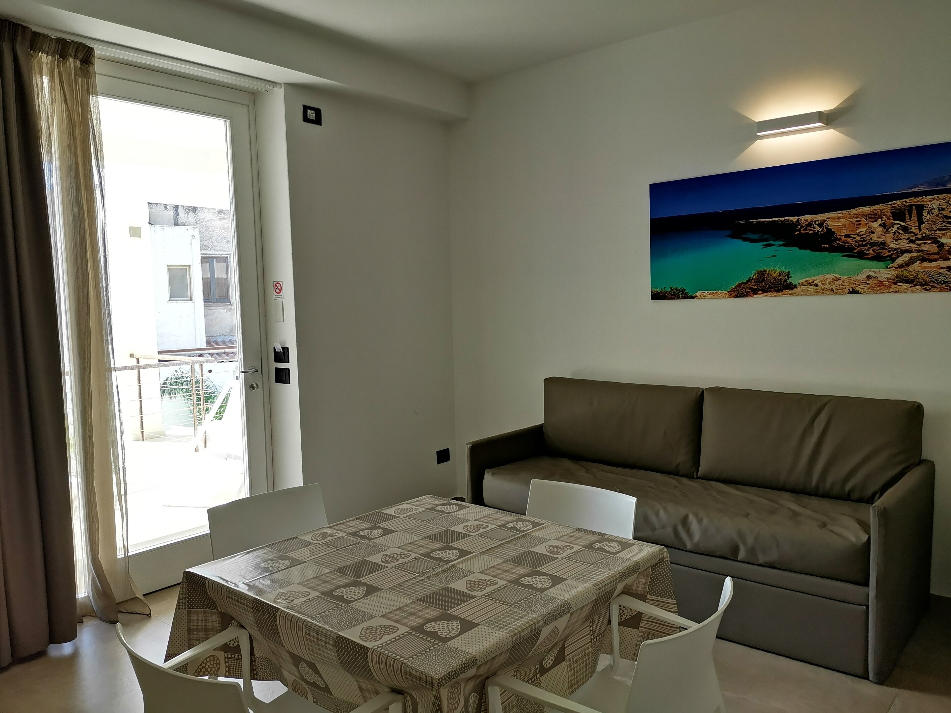 A room with a dining table, a sofa, and a painting of a coastal landscape.