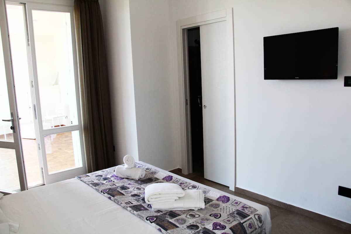 A hotel room with a bed, a TV mounted on the wall, and a door leading to a balcony.