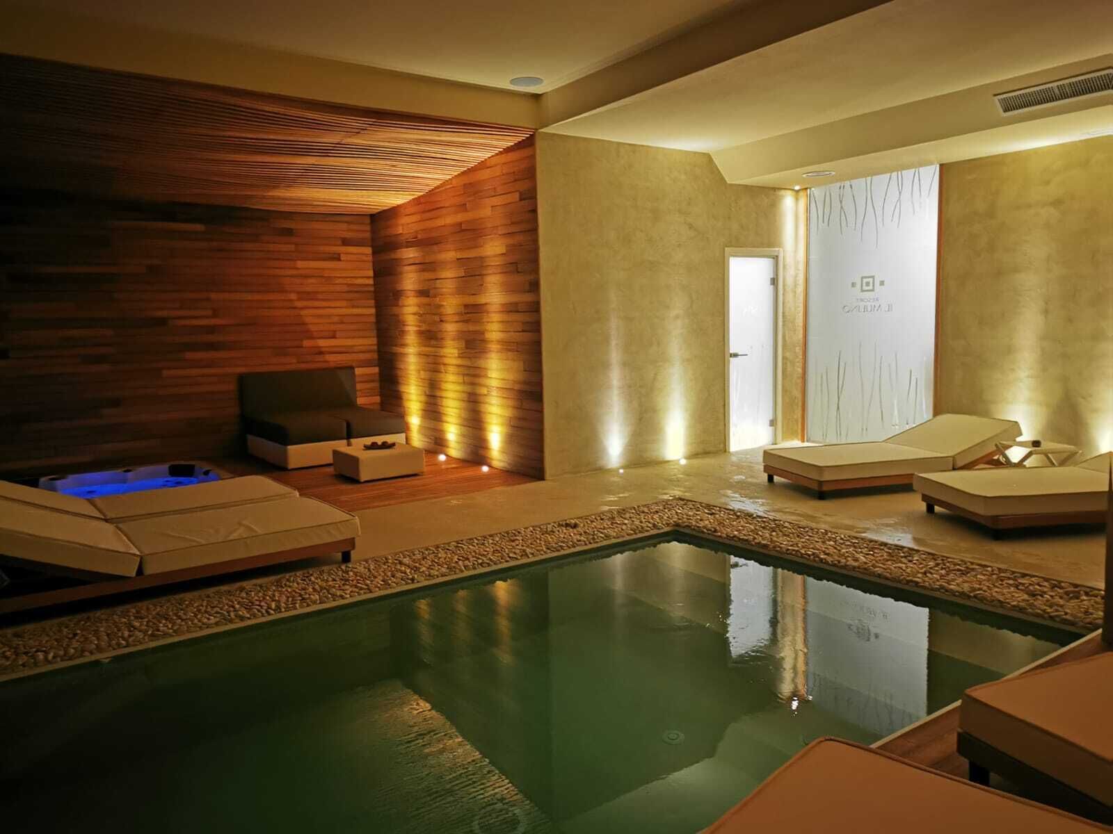 Ein moderner Poolbereich im Innenbereich mit Holzwand, einer Entspannungszone mit Liegestühlen und einem Spa-Raum mit Glastür.