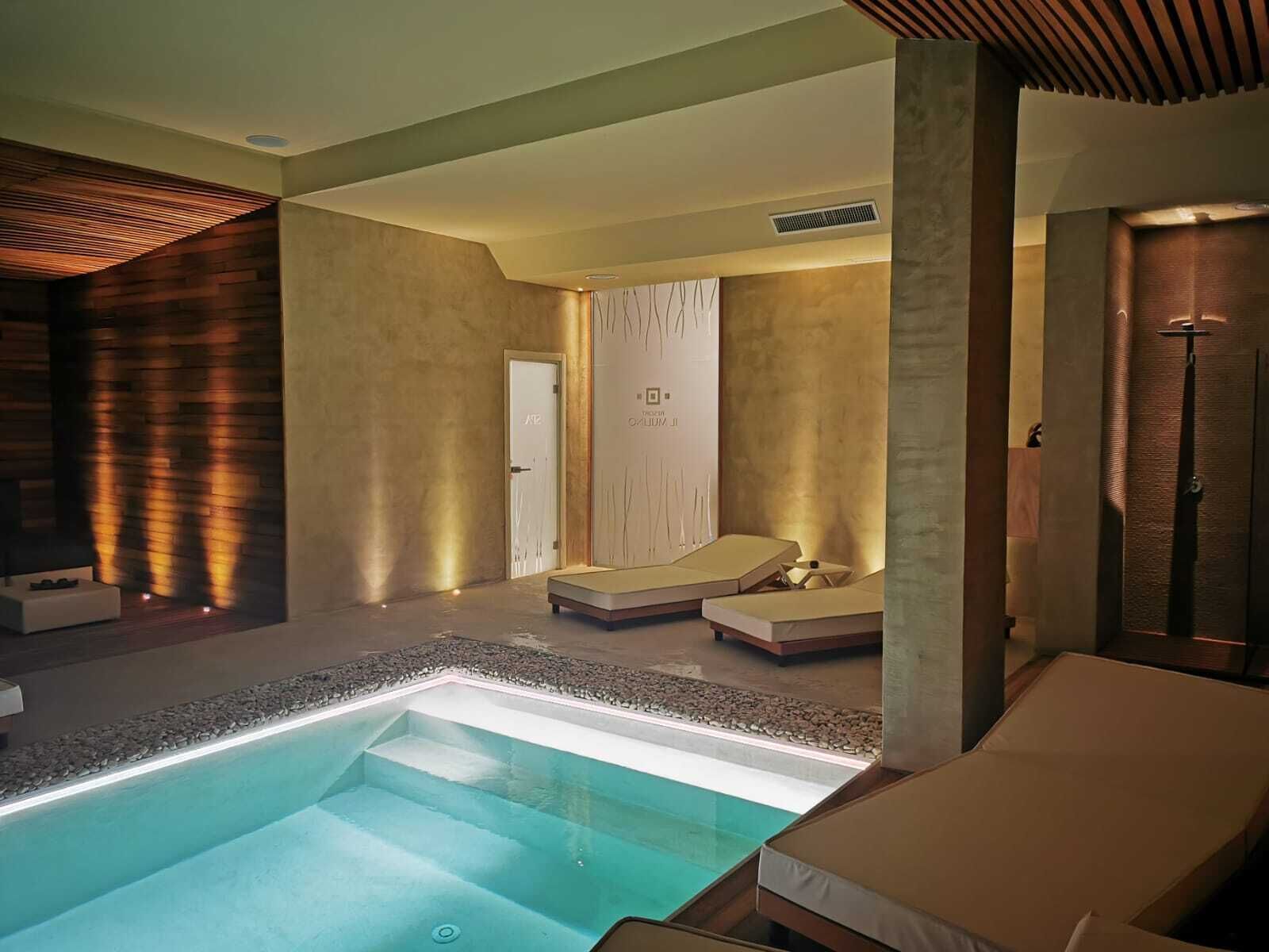 A modern spa room with a large pool, lounge chairs, and a wooden wall with vertical slats.
