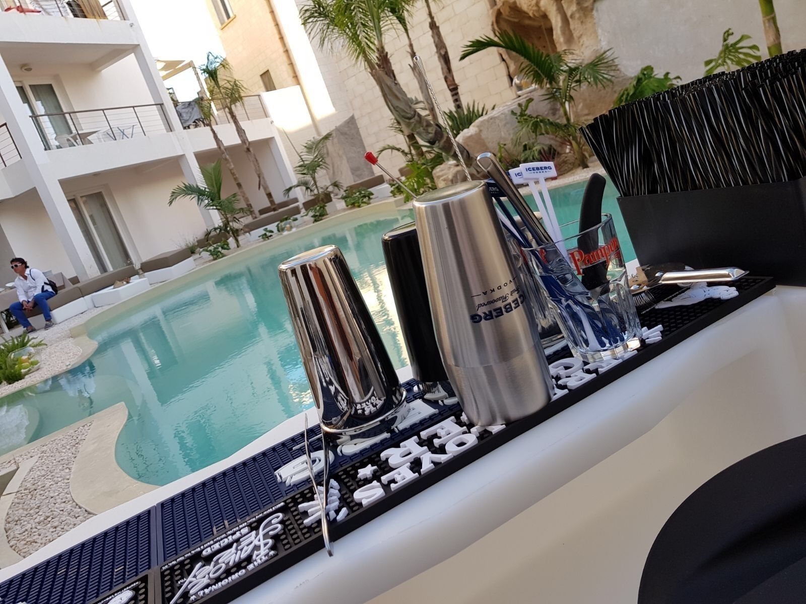 Ein Barbereich am Pool mit einem Barhocker, einem Metallbecher und einem Glas mit Trinkhalm.