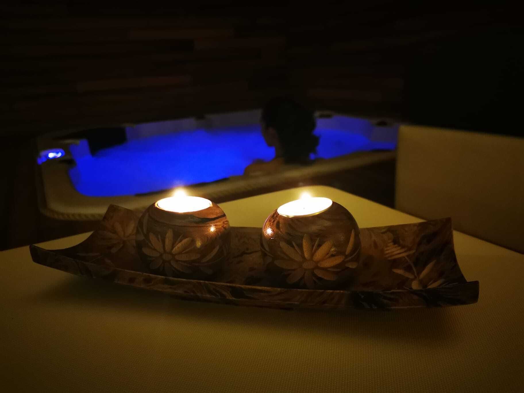 A dimly lit room with a wooden table featuring two candles. In the background, there is a blue-lit bathtub.