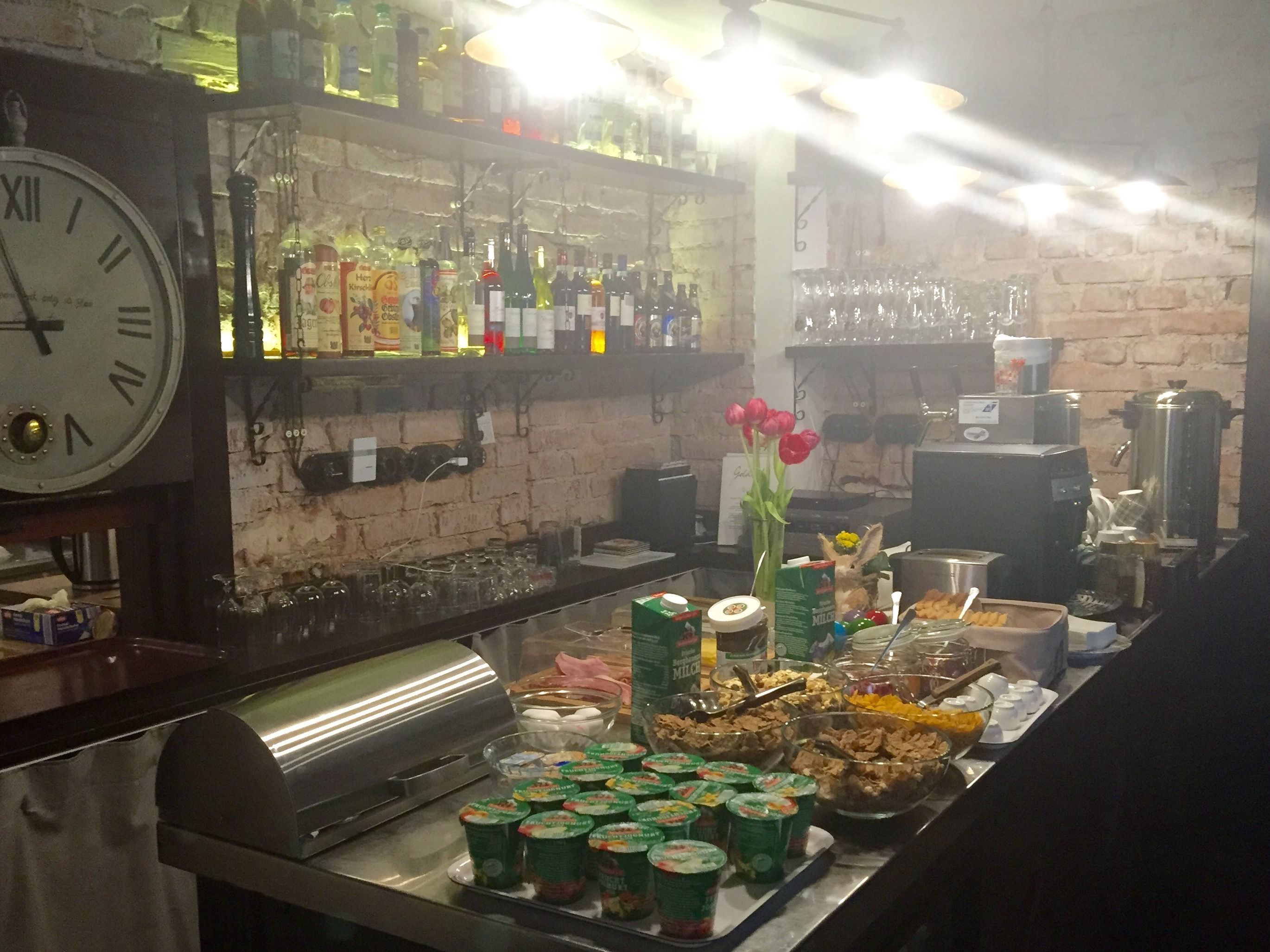 A bar area with a clock, shelves of bottles, and a buffet with food items.