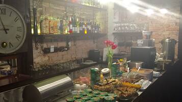 A bar area with a clock, shelves of bottles, and a buffet with food items.