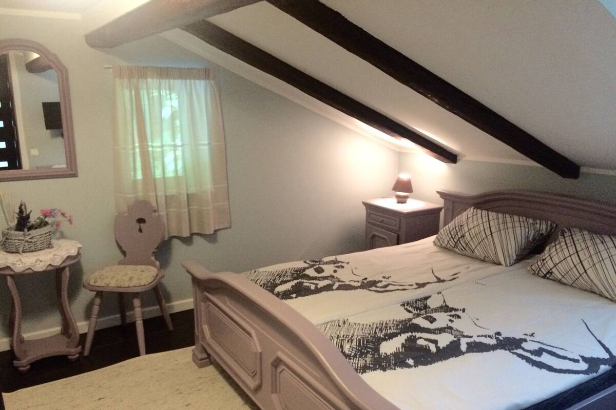 A bedroom with a bed, a nightstand, a chair, a dresser, a mirror, and a window with curtains.