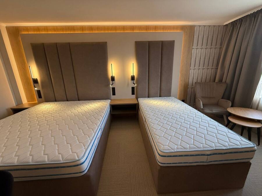 Une chambre d’hôtel avec deux lits simples, une table de chevet en bois, une petite table et une chaise.