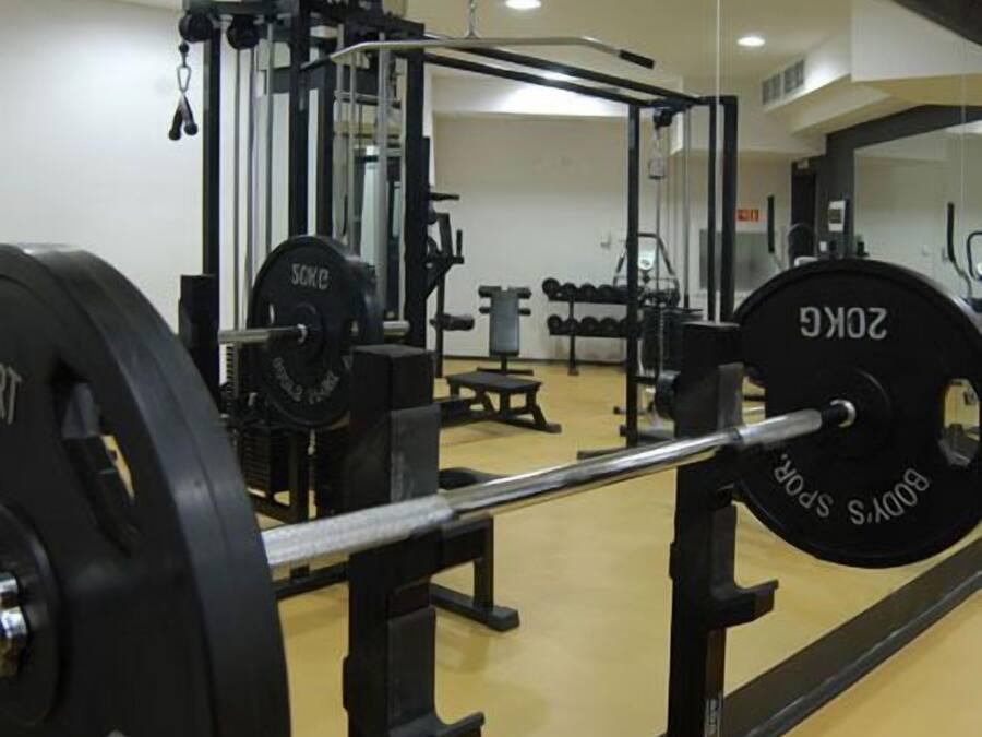 Un gimnasio con equipo de levantamiento de pesas, incluyendo barra con pesas y una estructura para sentadillas.
