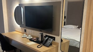 Habitación de hotel con escritorio de madera, televisor de pantalla plana, teléfono y espejo.