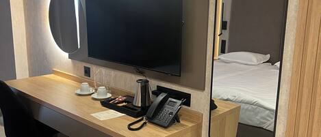 A hotel room with a wooden desk, a flat-screen TV, a telephone, and a mirror.