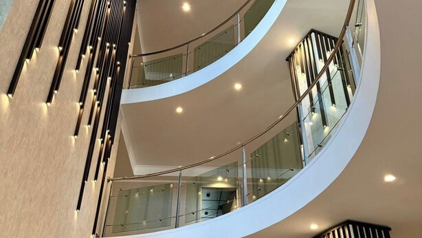 Un interior moderno con una escalera curva, barandillas de vidrio e iluminación empotrada.
