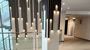 Un vestíbulo moderno con techo alto, una columna central con iluminación integrada, barandilla de vidrio y un sofá elegante.
