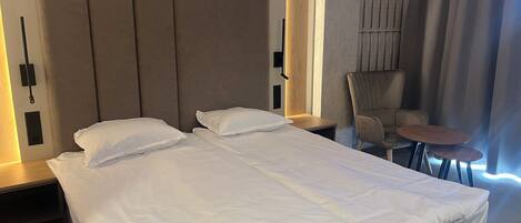 Una habitación de hotel con una cama grande, dos mesitas de noche, una silla y una pequeña mesa.