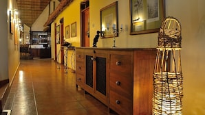 A hallway with wooden cabinets, a wicker lamp, and framed pictures on the wall. - Arumeru River Lodge (Arusha)
