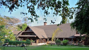 A traditional building with a sloped roof and a chimney, surrounded by a well-maintained lawn and trees. - Arumeru River Lodge (Arusha)
