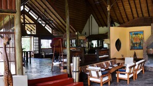 A spacious indoor area with a large fireplace, wooden furniture, and artwork on the walls. - Arumeru River Lodge (Arusha)