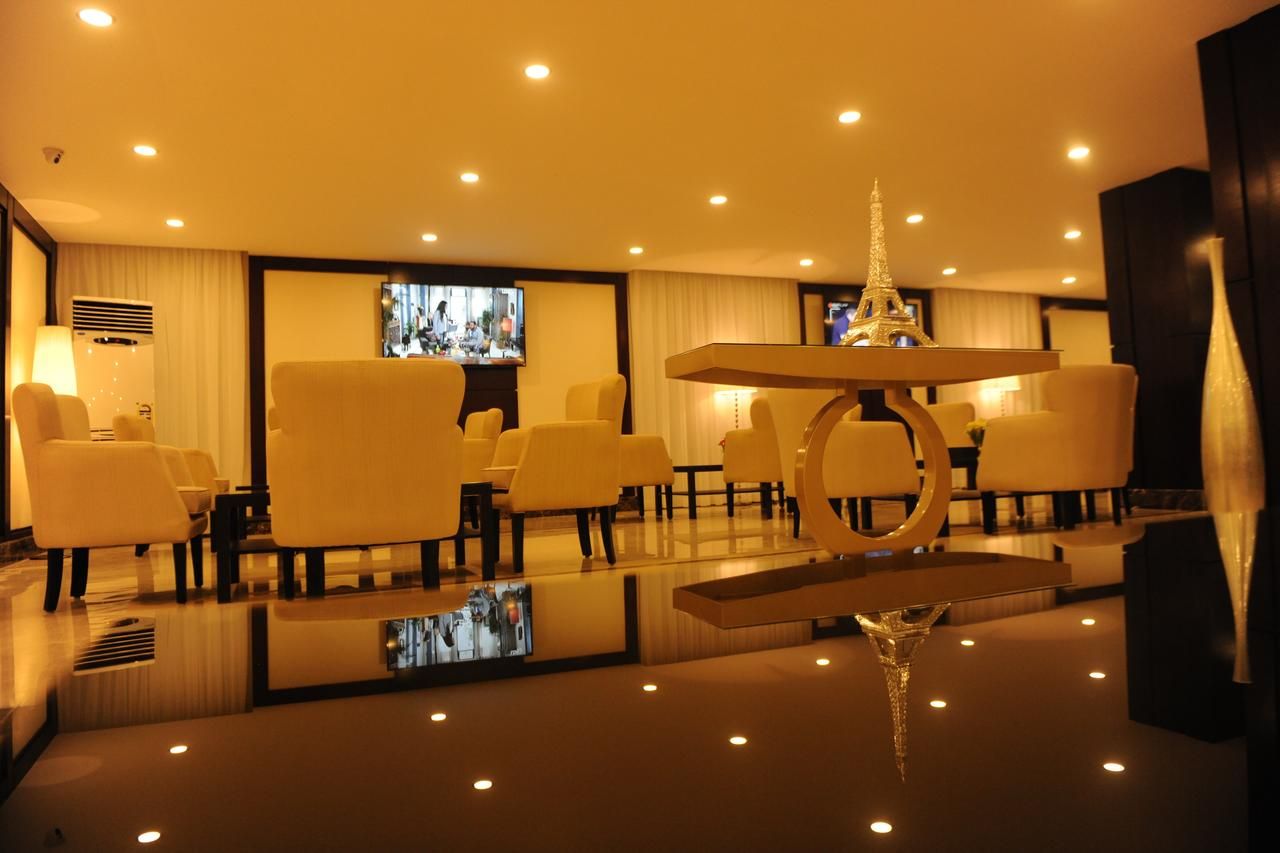 Vestíbulo de hotel con una mesa central, varias áreas de estar y una pantalla de televisión.