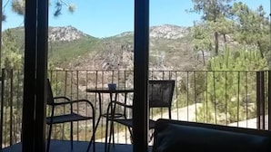 A balcony with a table and chairs, overlooking a mountainous landscape.