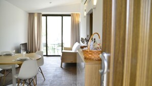 A modern hotel room with a dining area, a balcony, and a kitchenette.