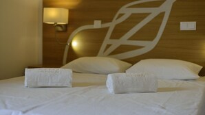 A neatly made bed with two rolled towels, a wall-mounted lamp, and a large abstract design on the headboard.