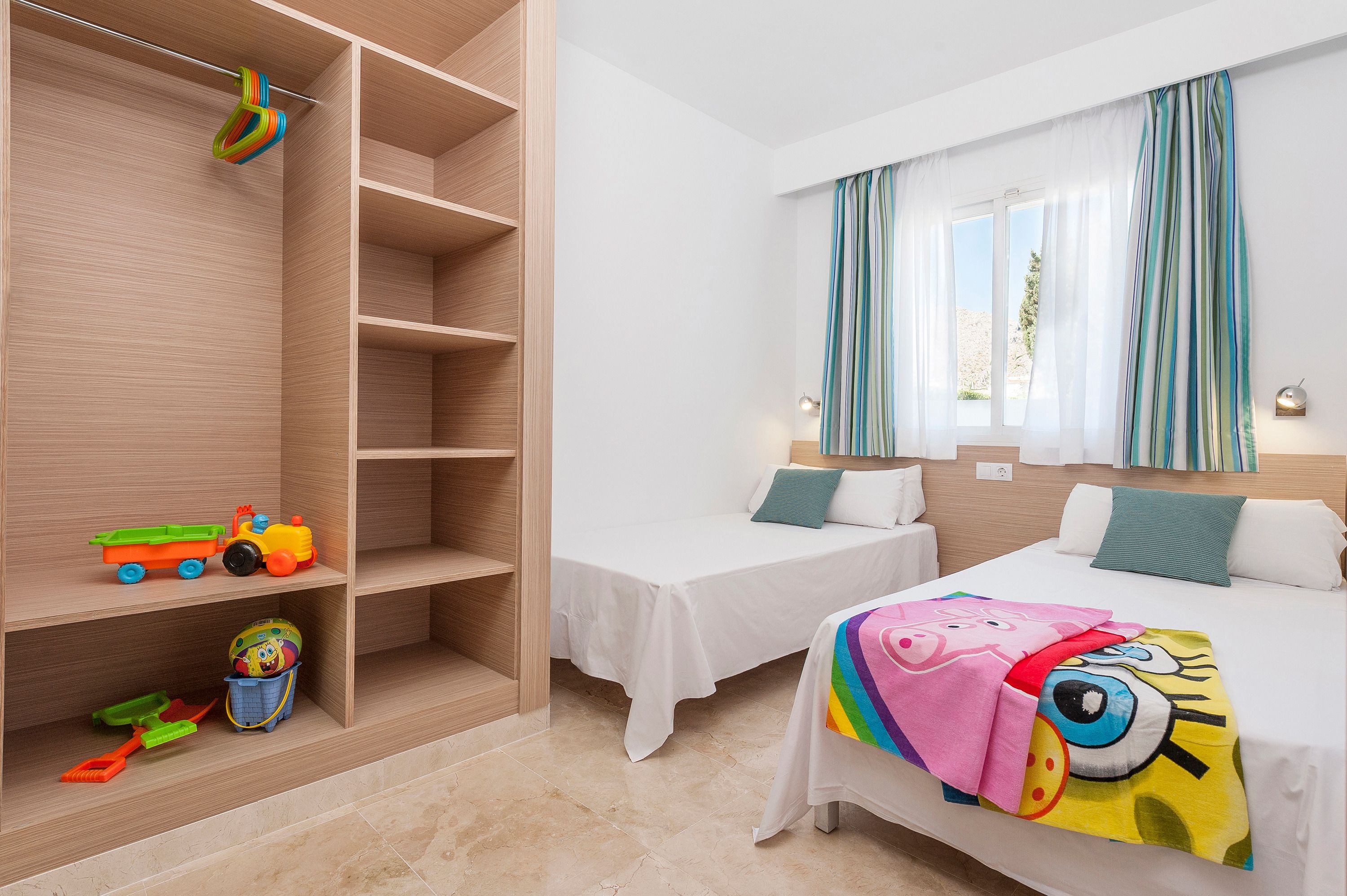 Een slaapkamer met twee bedden, een houten garderobe en een plank met kinderspeelgoed.