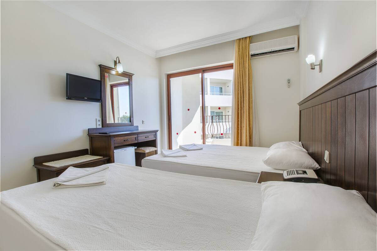A hotel room with two beds, a desk, a flat-screen TV, and a large window with a view of a building.