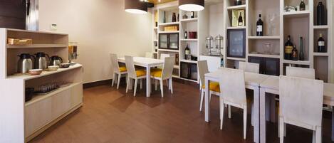 A modern kitchen with white cabinetry, a dining area with white chairs and yellow cushions, and a wine collection on shelves.